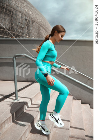 Full length shot of healthy young woman running down on steps and smiling. Female runner exercising on stairs Full length shot of healthy young woman running down on steps and smiling. Female runner exercising on stairs 139041624