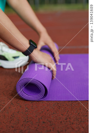 Individual Preparing to Roll up a Purple Yoga Mat After a Workout Session in an Outdoor Fitness Area at Sunset Individual Preparing to Roll up a Purple Yoga Mat After a Workout Session in an Outdoor Fitness Area at Sunset 139041689