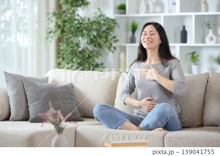 Happy asian woman doing breathing exercises on a couch 139041755