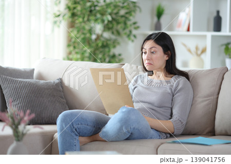 Perplexed asian woman checking incomprehensible documents at home Perplexed asian woman checking incomprehensible documents at home 139041756