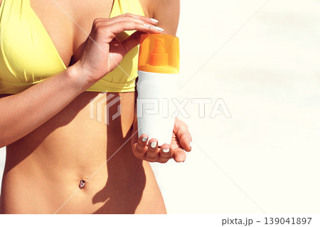 Beautiful young woman in yellow bikini offering protective cream on the beach under the sun Beautiful young woman in yellow bikini offering protective cream on the beach under the sun 139041897