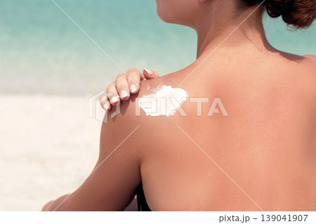 Woman applying sunscreen creme on tanned shoulder. Skincare. Body Sun protection suncream. Bikini hat woman applying moisturizing sunscreen lotion on back. Woman applying sunscreen creme on tanned shoulder. Skincare. Body Sun protection suncream. Bikini hat woman applying moisturizing sunscreen lotion on back. 139041907