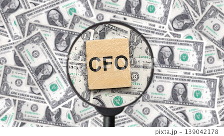 A wooden block with CFO text under a magnifying glass on a background of US dollar bills. Represents chief financial officer, accounting, auditing, and corporate finance management A wooden block with CFO text under a magnifying glass on a background of US dollar bills. Represents chief financial officer, accounting, auditing, and corporate finance management 139042178