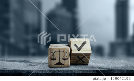 Wooden cubes with justice scale and checkmark icons on a grey surface. Concept of legal ethics, business compliance, and corporate responsibility with a blurred city background Wooden cubes with justice scale and checkmark icons on a grey surface. Concept of legal ethics, business compliance, and corporate responsibility with a blurred city background 139042196