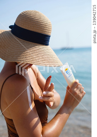 Attractive Woman Holding Sunscreen Bottle And Applying Sun Cream On Shoulder At Beach. Beauty Skincare And Sun Protection Routine During Summer Vacation 139042715
