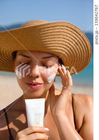 Beautiful Woman Applying Sunscreen On Face And Holding Bottle At Beach. Beauty Skincare And Sun Protection Concept. Female Using Sun Cream 139042767