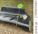 Fishing gear and container set on a bench at a park during the day with grass nearby 139043083