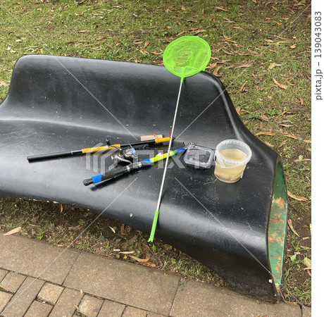 Fishing gear and container set on a bench at a park during the day with grass nearby 139043083