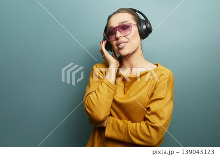 Woman listens to music with headphones while smiling in a studio against a plain blue backdrop during daytime Woman listens to music with headphones while smiling in a studio against a plain blue backdrop during daytime 139043123