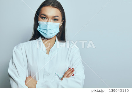 Health worker wearing a mask stands with arms crossed in a clinical setting during the day 139043150