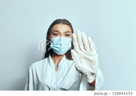 Woman in medical mask and gloves raises hand for safety during health awareness campaign in clinic setting 139043155