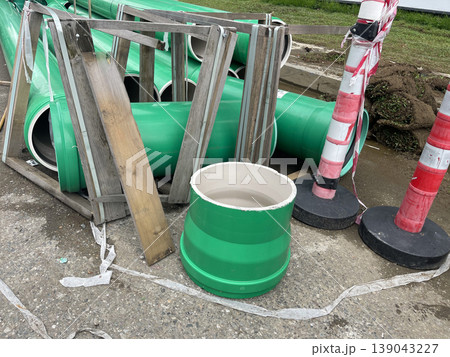 Construction site shows green pipes, wooden frames, and traffic cones in a work area during day time 139043227