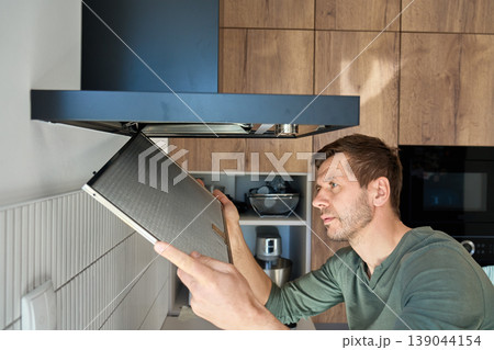Man removing filter from kitchen range hood for cleaning 139044154