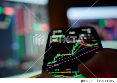 Investor trading stocks on mobile app with market screens Investor trading stocks on mobile app with market screens 139044165