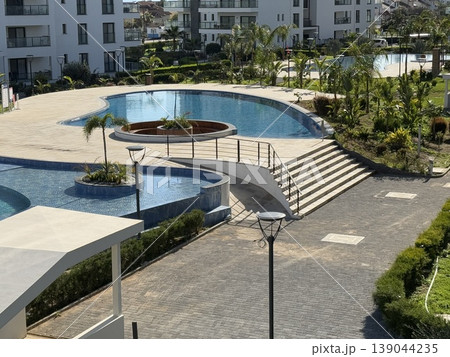 Swimming pool in modern apartment complex with landscaped greenery and pathways Swimming pool in modern apartment complex with landscaped greenery and pathways 139044235