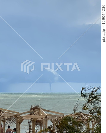 Tropical beach with distant waterspout and partly cloudy sky, includes background and copy space 139044236