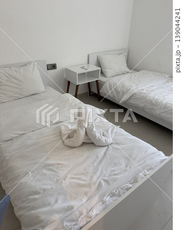 Two neatly made beds with white linens and towel swan centerpiece in hotel room background Two neatly made beds with white linens and towel swan centerpiece in hotel room background 139044241