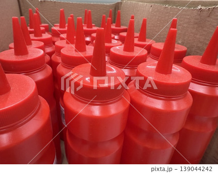 Red plastic ketchup bottles with pointed caps stacked in cardboard box, suitable for background Red plastic ketchup bottles with pointed caps stacked in cardboard box, suitable for background 139044242