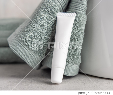 White blank eye cream tube mockup near light green bath towel. Cosmetic skincare product packaging White blank eye cream tube mockup near light green bath towel. Cosmetic skincare product packaging 139044543