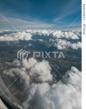 Aerial view of dense clouds above countryside from airplane window Aerial view of dense clouds above countryside from airplane window 139044808