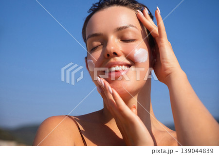 Beautiful Woman Smiling And Touching Face With Sunscreen At Beach. Beauty Skincare Concept. Female Using Sun Cream Beautiful Woman Smiling And Touching Face With Sunscreen At Beach. Beauty Skincare Concept. Female Using Sun Cream 139044839