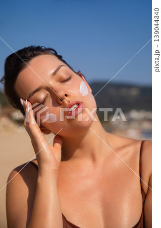 Young Woman With Sunscreen On Face And Looking At Camera At Beach. Beauty Skincare And Sun Protection Concept Young Woman With Sunscreen On Face And Looking At Camera At Beach. Beauty Skincare And Sun Protection Concept 139044840