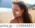 Beauty Woman Turning Back With Sunscreen On Face At Beach. Skincare And Sun Protection Concept. Female Using Sun Cream For Healthy Skin 139044852