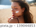 Young Woman With Sunscreen On Face Looking Down At Beach. Beauty Skincare And Sun Protection Concept. Female Using Sun Cream Lotion 139044853