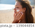 Attractive Woman Applying Sunscreen On Cheek At Beach. Beauty Skincare And Sun Protection Concept. Female Using Sun Cream Lotion 139044854