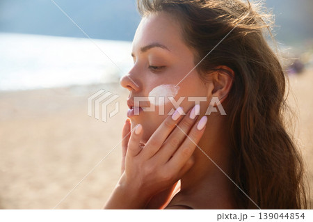 Attractive Woman Applying Sunscreen On Cheek At Beach. Beauty Skincare And Sun Protection Concept. Female Using Sun Cream Lotion 139044854