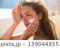 Beautiful Woman Applying Sunscreen On Face With Hands At Beach. Beauty Skincare Concept. Female Using Sun Cream For Skin Protection 139044855