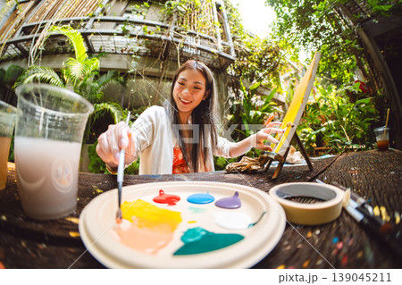 Portrait of happy young adult asian woman painting brush on canvas at workshop art lesson class. 139045211