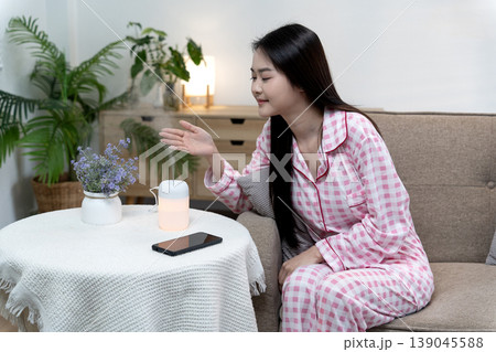 Asian adult woman relaxing at home enjoying humidifier mist for wellness lifestyle and comfortable self care moment creating tranquil peaceful cozy atmosphere in modern living room Asian adult woman relaxing at home enjoying humidifier mist for wellness lifestyle and comfortable self care moment creating tranquil peaceful cozy atmosphere in modern living room 139045588