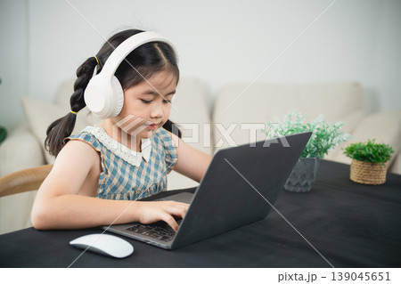 Young girl wearing headphones focused on laptop in modern interior, engaging with technology while studying or enjoying online activities at home Young girl wearing headphones focused on laptop in modern interior, engaging with technology while studying or enjoying online activities at home 139045651