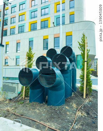 Pipes arranged in a cluster near a modern building with colorful windows in an urban area during daylight 139045809