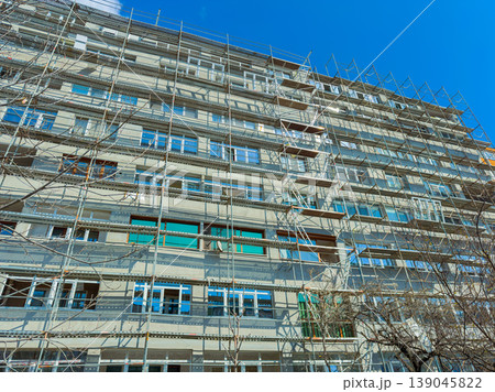 Construction work is taking place on a large building with scaffolding under a clear blue sky during daytime in an urban area Construction work is taking place on a large building with scaffolding under a clear blue sky during daytime in an urban area 139045822
