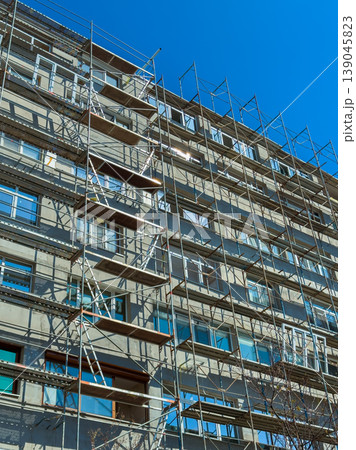 Construction work on a multi-story building with scaffolding under a clear blue sky during the day Construction work on a multi-story building with scaffolding under a clear blue sky during the day 139045823