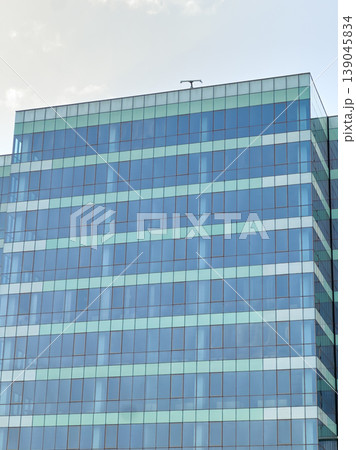 Modern office building with glass exterior in urban area during daytime showing multiple windows and reflections on the surface Modern office building with glass exterior in urban area during daytime showing multiple windows and reflections on the surface 139045834