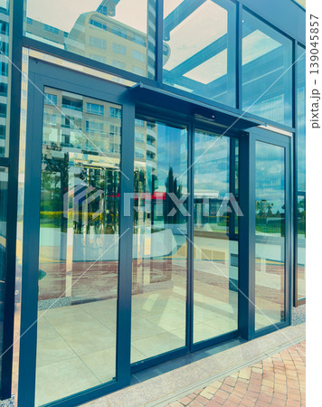 Modern glass entrance of a building showing reflection and surroundings in the afternoon light with clear skies and urban setting Modern glass entrance of a building showing reflection and surroundings in the afternoon light with clear skies and urban setting 139045857