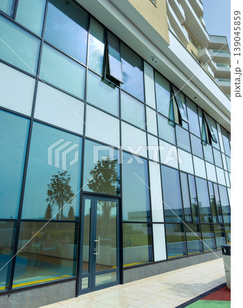 Building with large glass windows and open framework in a modern city on a sunny day with trees in the background 139045859