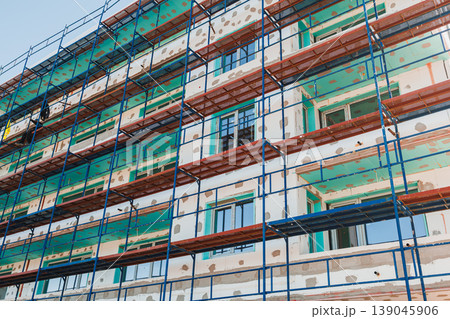Construction workers are working on a building facade in a city during daylight hours with scaffolding set up for access 139045906