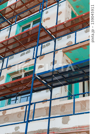 Workers perform construction activities on a building with scaffolding and incomplete exterior finishing in the afternoon hours Workers perform construction activities on a building with scaffolding and incomplete exterior finishing in the afternoon hours 139045911