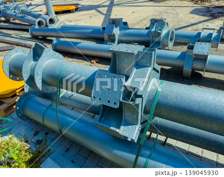 Steel pipes are stacked at a construction site during daytime with clear sky and scattered materials nearby for a large project 139045930