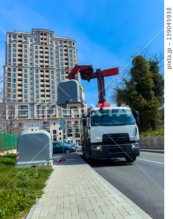Truck lifts garbage bin on street in urban area near tall building under clear blue sky during daylight hours 139045938
