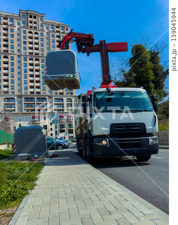 Garbage truck removes waste containers on city street during clear day 139045944