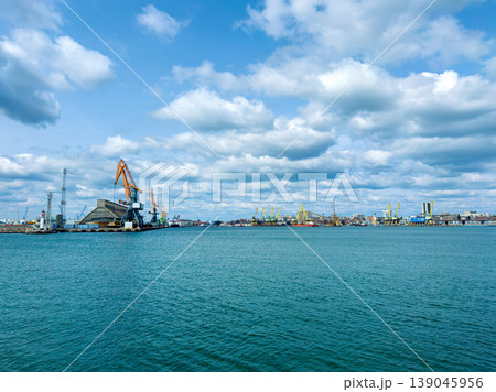 Vessels and cranes work at a busy harbor along the waterfront under a cloudy sky during daylight hours in a port city Vessels and cranes work at a busy harbor along the waterfront under a cloudy sky during daylight hours in a port city 139045956