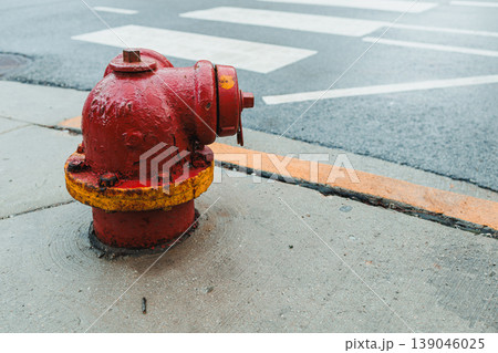 Fire hydrant located on a city sidewalk next to a street crossing in the late afternoon light with a wet pavement 139046025