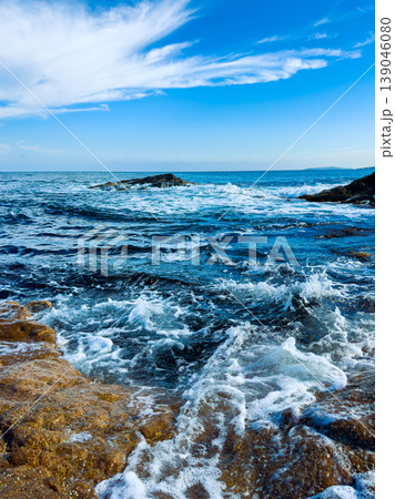 Waves crash on rocks at the shoreline with bright blue sky and distant horizon during daytime Waves crash on rocks at the shoreline with bright blue sky and distant horizon during daytime 139046080