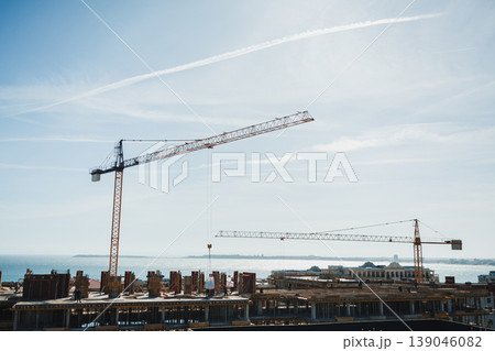 Construction site with cranes and new building under development near the coast during daylight hours Construction site with cranes and new building under development near the coast during daylight hours 139046082