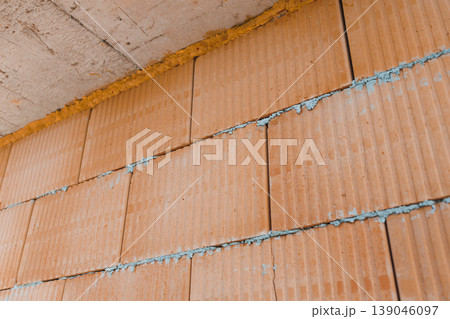 Construction of a wall with orange bricks and blue mortar filling the gaps at a building site in the afternoon sunlight 139046097